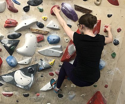 Ein Mädchen hängt an einer Boulderwand. Sie ist von hinten zu sehen. 