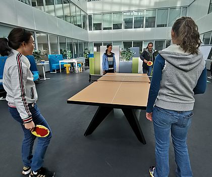 Zwei Mädchen sieht man mit dem Rücken, da sie gerade auf eine Tischtennisplatte schauen und den Ball von der anderen Seite erwarten. 