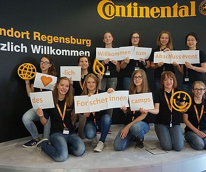 11 Mädchen halten gemeinsam ein Schild hoch auf dem steht "Willkommen zum Abschlussevent des Forscherinnen-Camps"