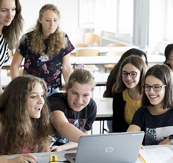 Forscherinnen-Camp Man sieht mehrere Mädchen, die freudig auf einen Laptop in der Mitte zeigen.